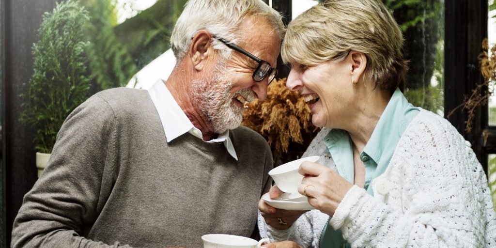 Afbeelding van een man en vrouw boven de 55 beide lachend met een kopje koffie