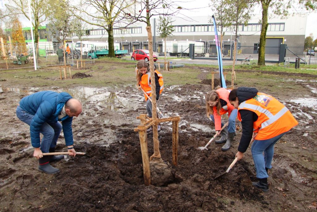 Afbeelding van wethouder Dorus Klomberg die samen met de kinderen van de basisschool Prinses Margrietschool uit Spankeren, de eerste boom plant op de buurspeelplaats