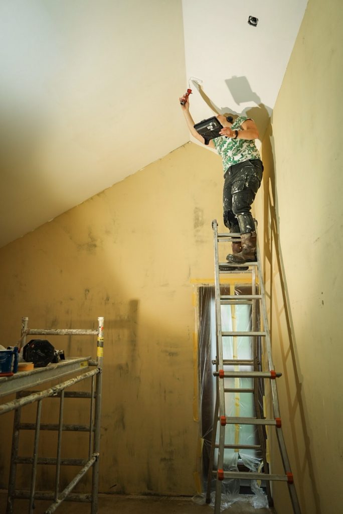 Klusser werkt vanaf een ladder aan de met leem gestucte binnenwand